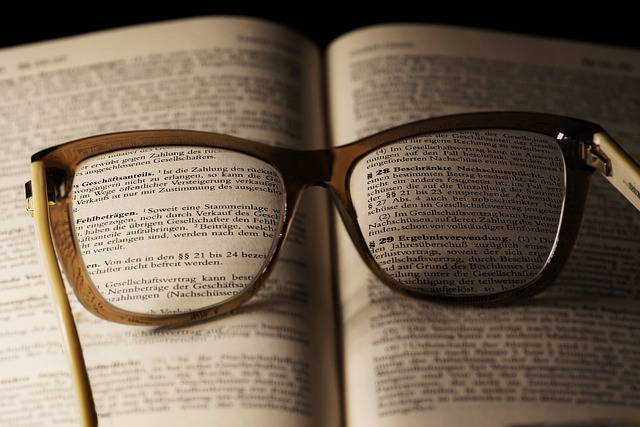 Auf einem aufgeschlagenen Gesetzbuch liegt eine Brille, durch dessen Gläser Teile des Textes lesbar werden